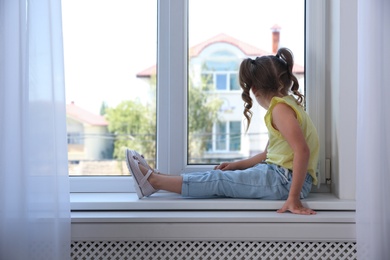 Cute little girl on window sill at home