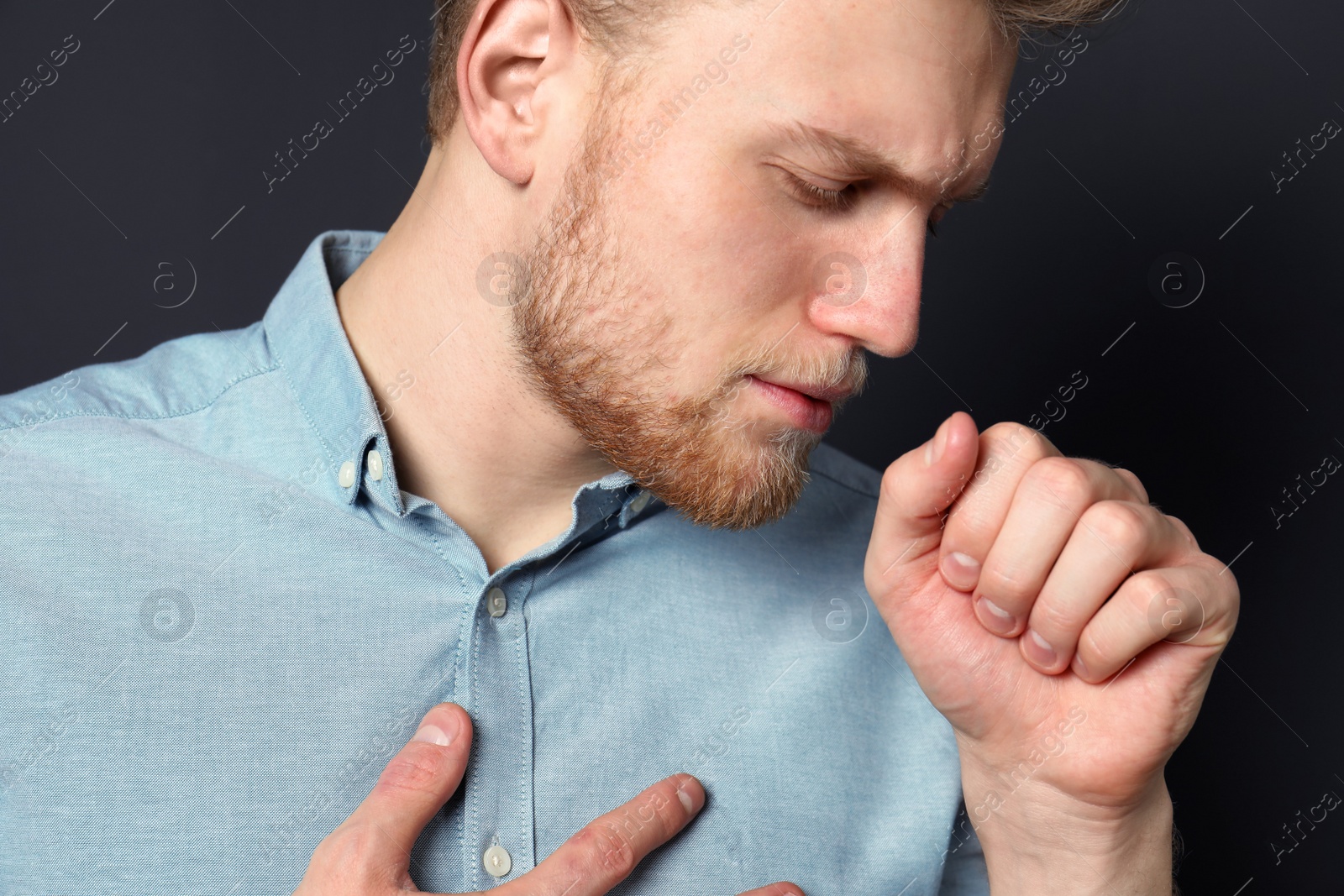 Photo of Handsome young man coughing against dark background