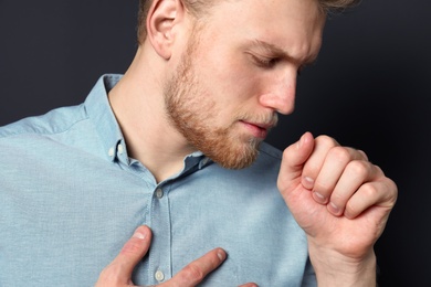 Handsome young man coughing against dark background