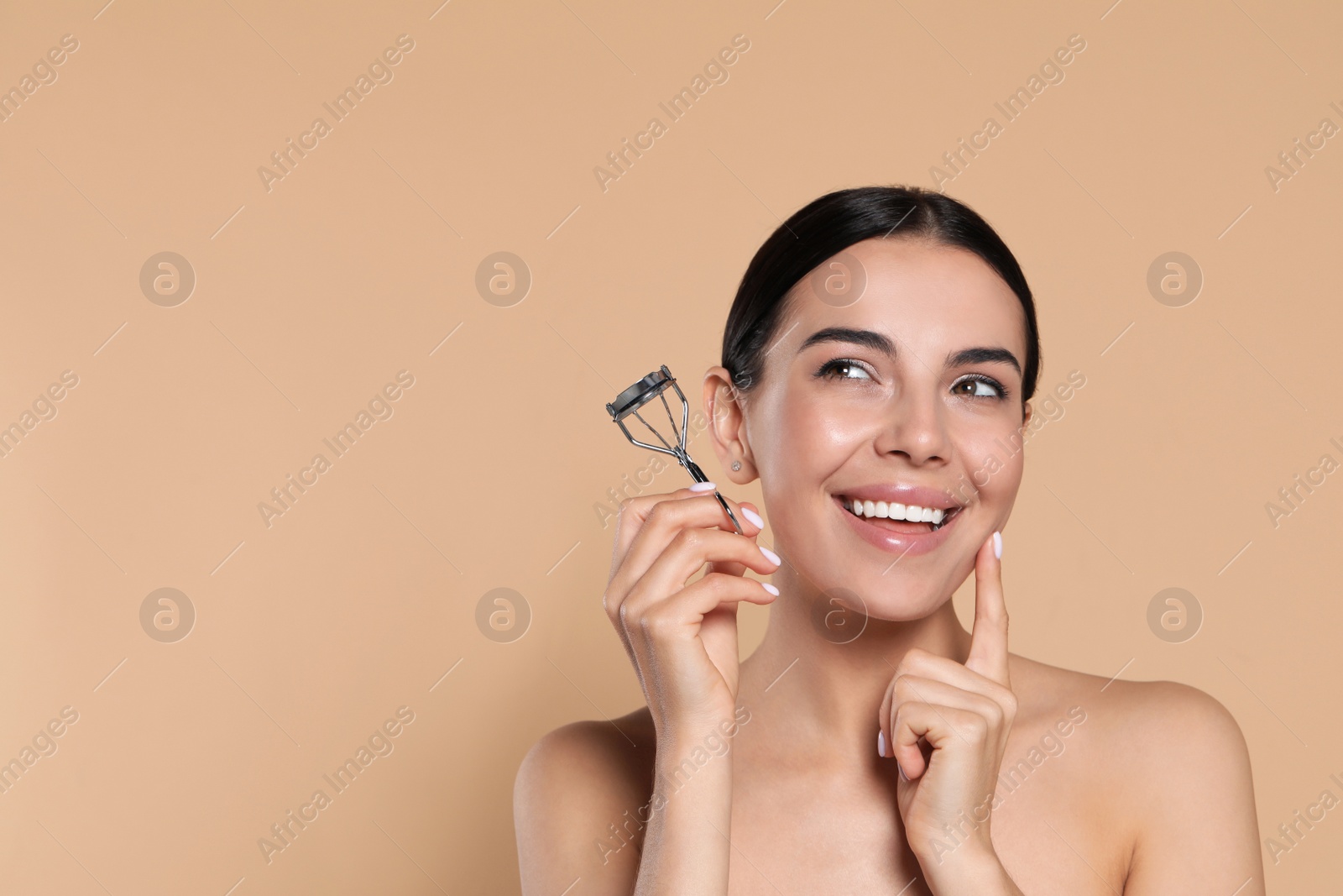 Photo of Emotional young woman with eyelash curler on beige background, space for text