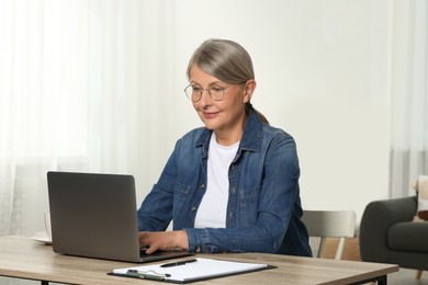 Photo of Beautiful senior woman using laptop at wooden table indoors