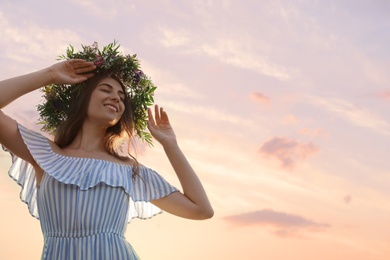 Young woman wearing wreath made of beautiful flowers outdoors on sunny day