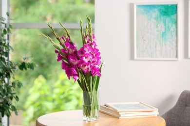 Photo of Vase with beautiful pink gladiolus flowers on wooden table in room, space for text