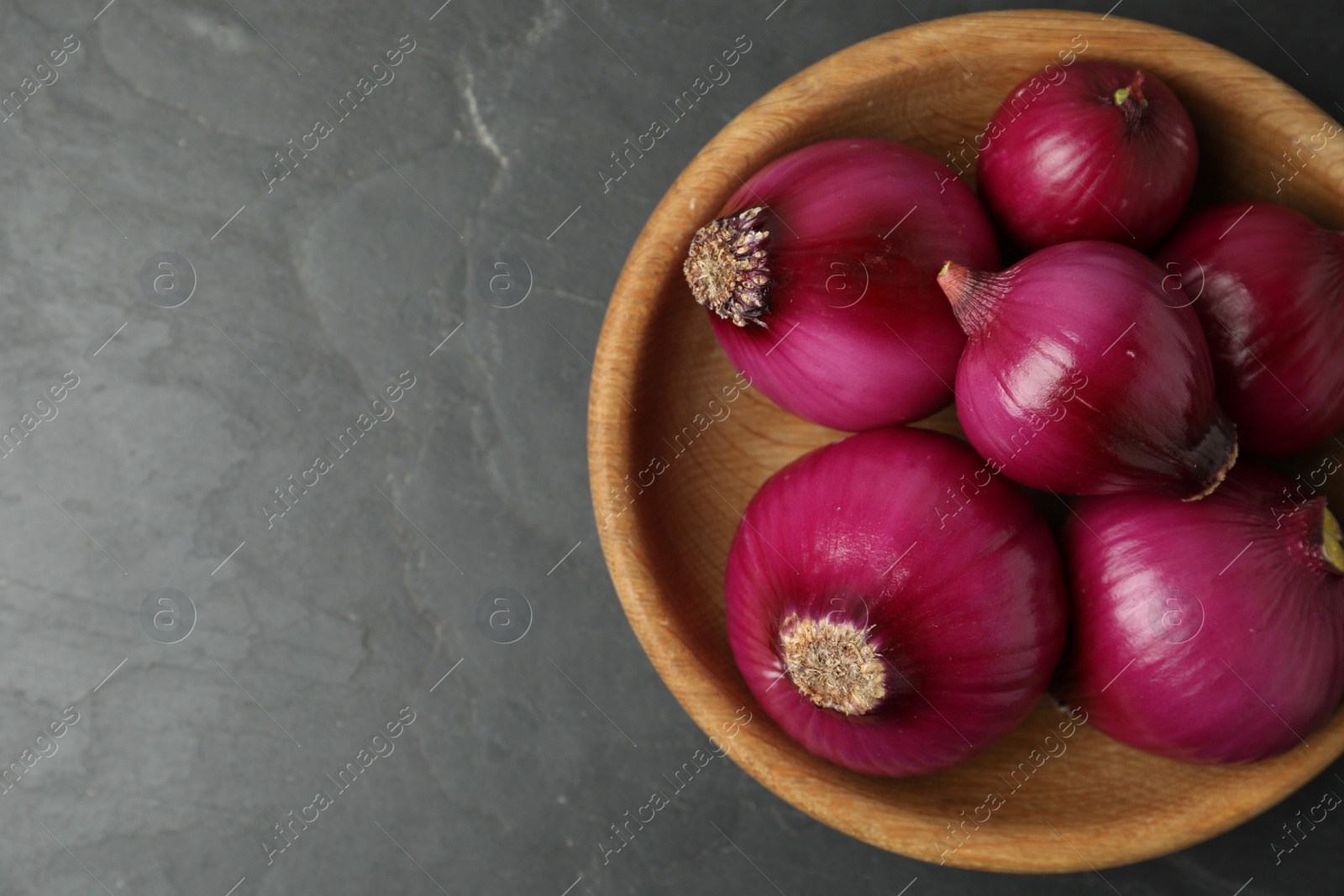 Photo of Ripe red onion bulbs in wooden bowl on black table, top view. Space for text