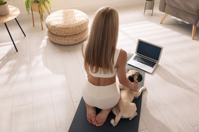Photo of Woman with dog watching online yoga class at home, back view