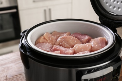 Photo of Fresh cut chicken in modern multi cooker on table, closeup