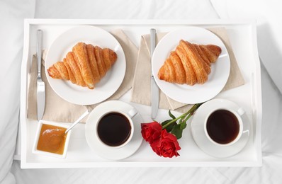 Photo of Tasty breakfast served in bed. Fresh croissants, coffee and honey on tray, top view