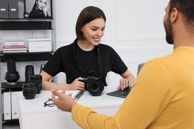 Young professional photographer holding camera while talking with man in modern photo studio