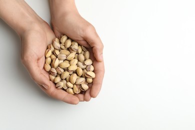 Woman holding tasty roasted pistachio nuts on white background, top view. Space for text