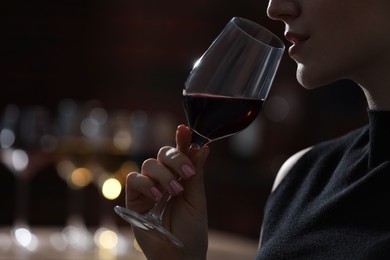 Woman with glass of red wine against blurred background, closeup. Space for text