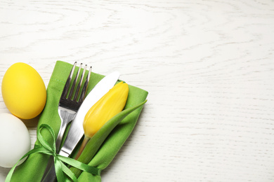 Photo of Cutlery set and eggs on white wooden table, flat lay with space for text. Easter celebration