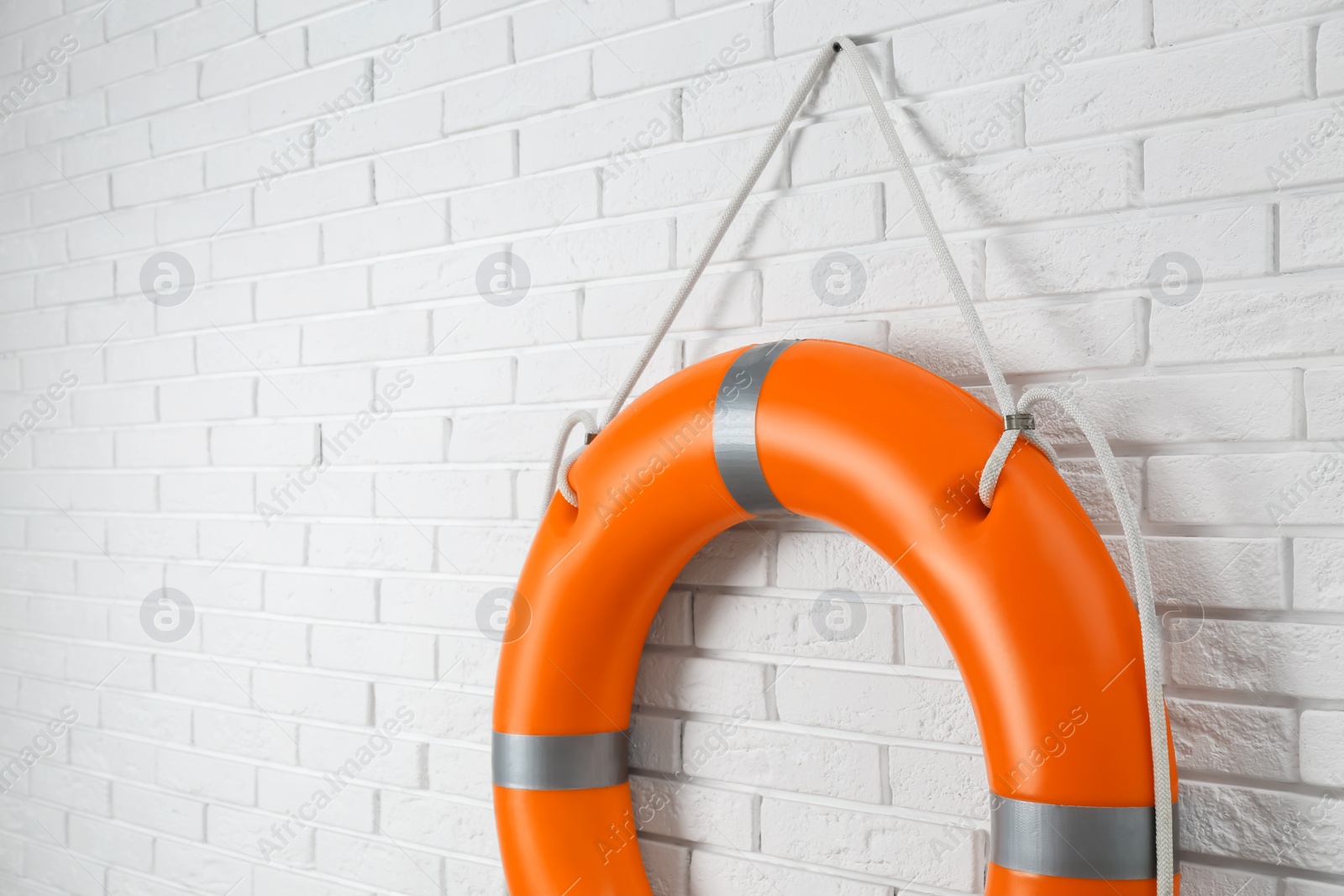 Photo of Orange lifebuoy and space for text on white brick wall. Rescue equipment