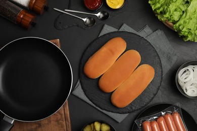Photo of Different tasty ingredients for hot dog and pan on dark table, flat lay