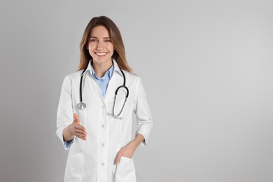 Happy female doctor offering handshake on light grey background. Space for text