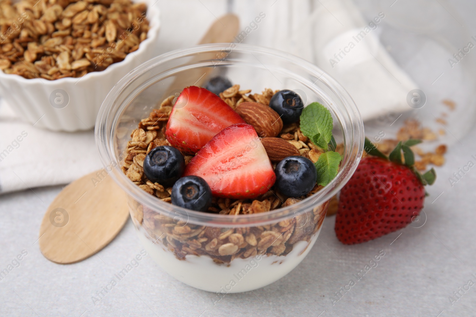 Photo of Tasty granola with berries, nuts and yogurt in plastic cup on light table, closeup