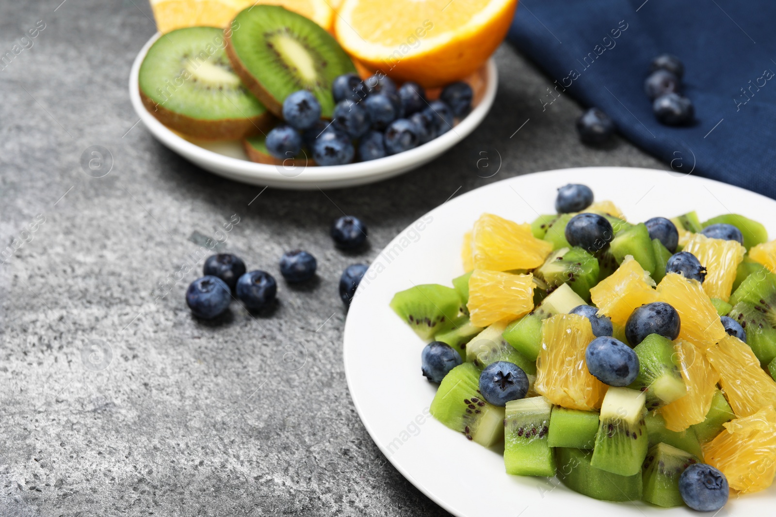 Photo of Plate of tasty fruit salad on grey textured table, closeup