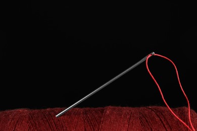 Photo of Red sewing thread with needle on black background, closeup