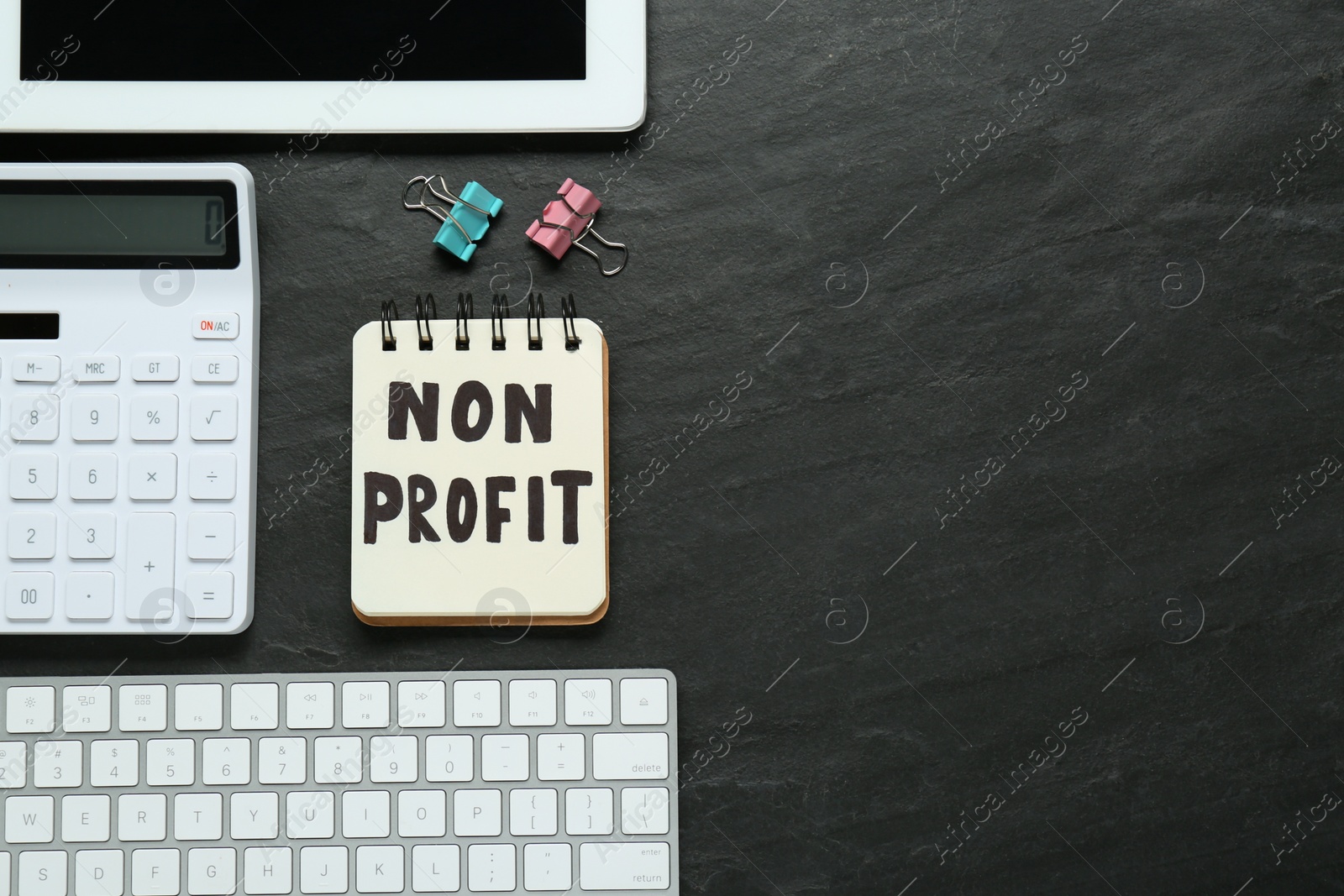 Photo of Notebook with phrase Non Profit, calculator and computer keyboard on black table, flat lay. Space for text