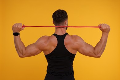 Photo of Young man exercising with elastic resistance band on orange background, back view