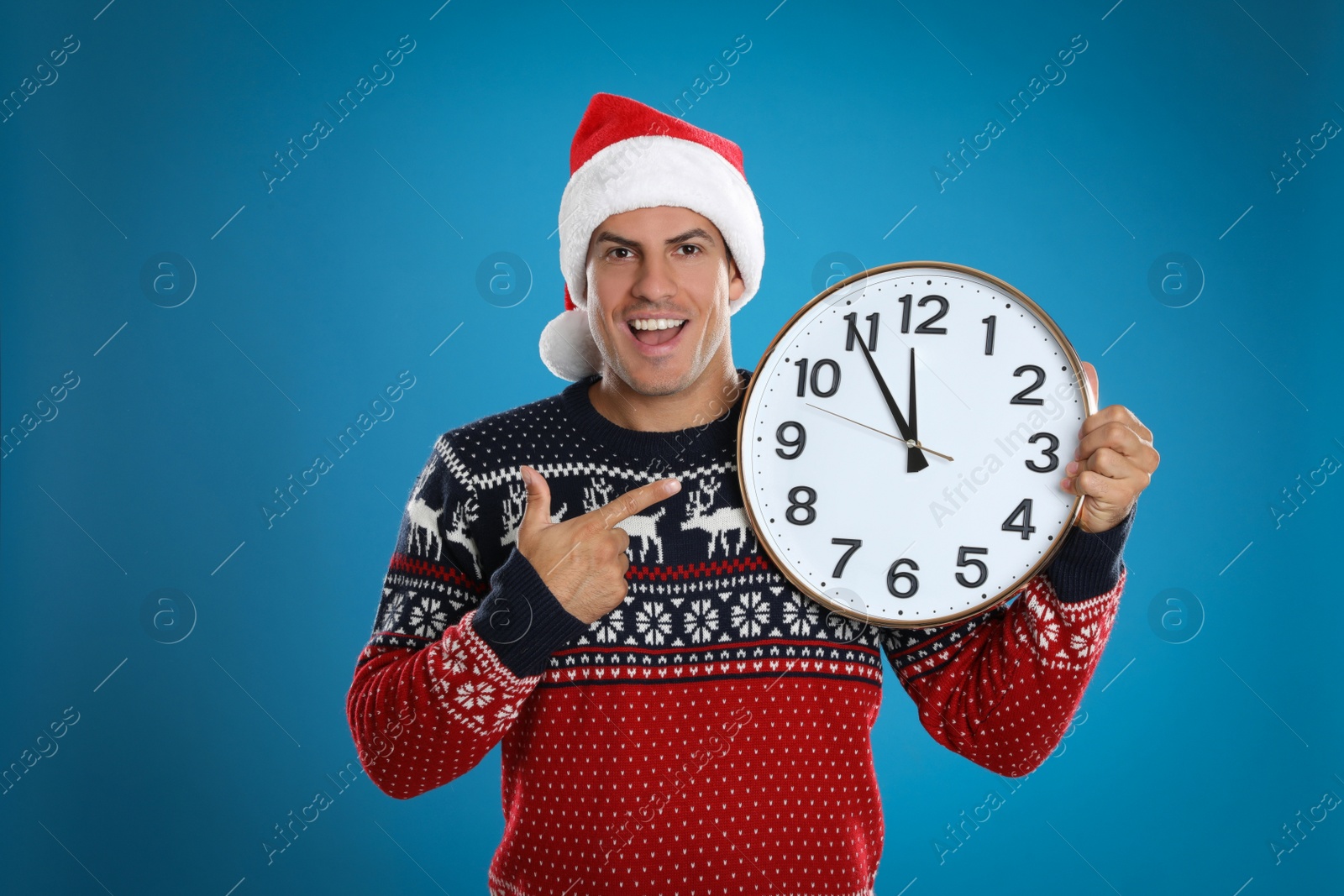 Photo of Man in Santa hat with clock on blue background. New Year countdown