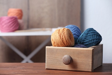 Photo of Colorful clews of threads in drawer on wooden table against blurred background, space for text