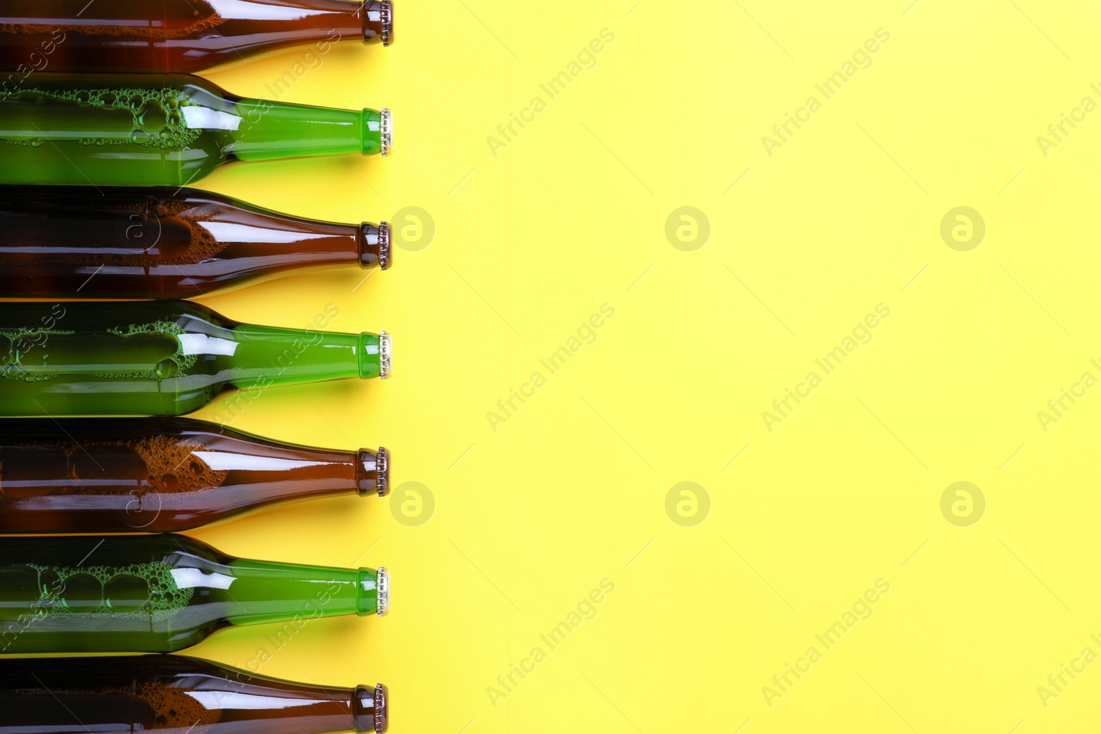 Photo of Bottles of beer on yellow background, flat lay. Space for text