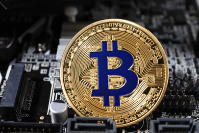 Photo of Golden bitcoin on computer circuit board, closeup. Digital currency