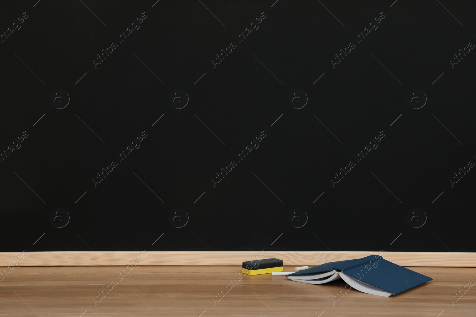 Photo of Open book, pieces of chalk and duster on wooden table near blackboard, space for text