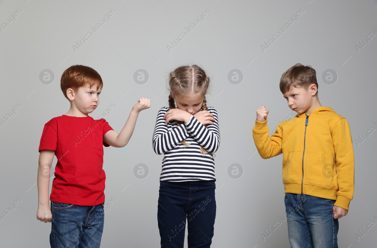 Photo of Boys with clenched fists looking at girl on light grey background. Children's bullying