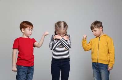 Photo of Boys with clenched fists looking at girl on light grey background. Children's bullying