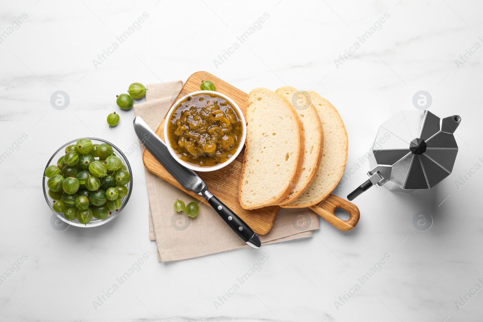 Photo of Delicious gooseberry jam, bread, fresh berries and coffee maker on white table, flat lay