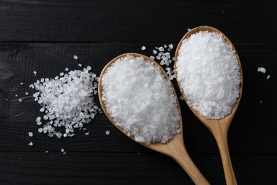 Photo of Organic salt in spoons on black wooden table, top view