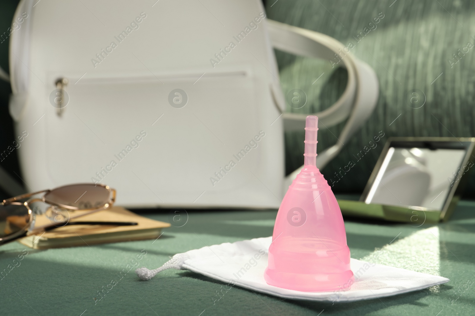 Photo of Pink menstrual cup with bag and different women's accessories on green sofa, space for text