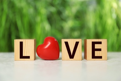 Photo of Word Love made of wooden cubes with letters and red decorative heart on light table