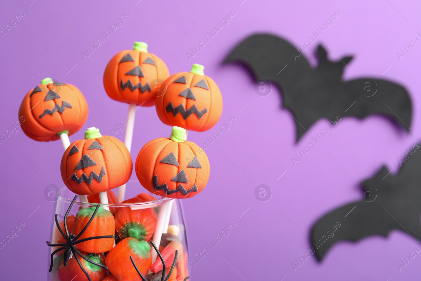 Photo of Delicious Halloween themed cake pops on violet background, closeup. Space for text