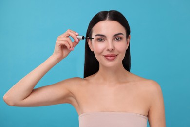 Photo of Beautiful woman applying serum onto her eyelashes on light blue background. Cosmetic product