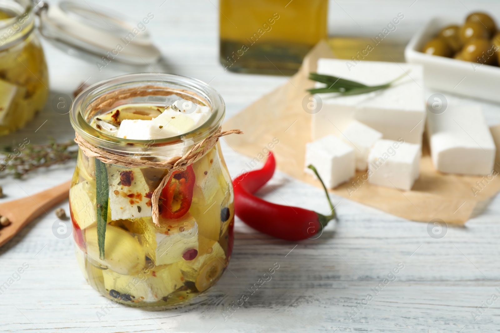 Photo of Jar with feta cheese marinated in oil on white wooden table. Pickled food