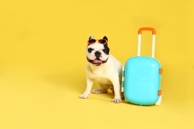 Photo of French bulldog with sunglasses and little suitcase on yellow background. Space for text