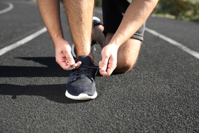 Sporty man tying shoelaces outdoors on sunny morning, closeup