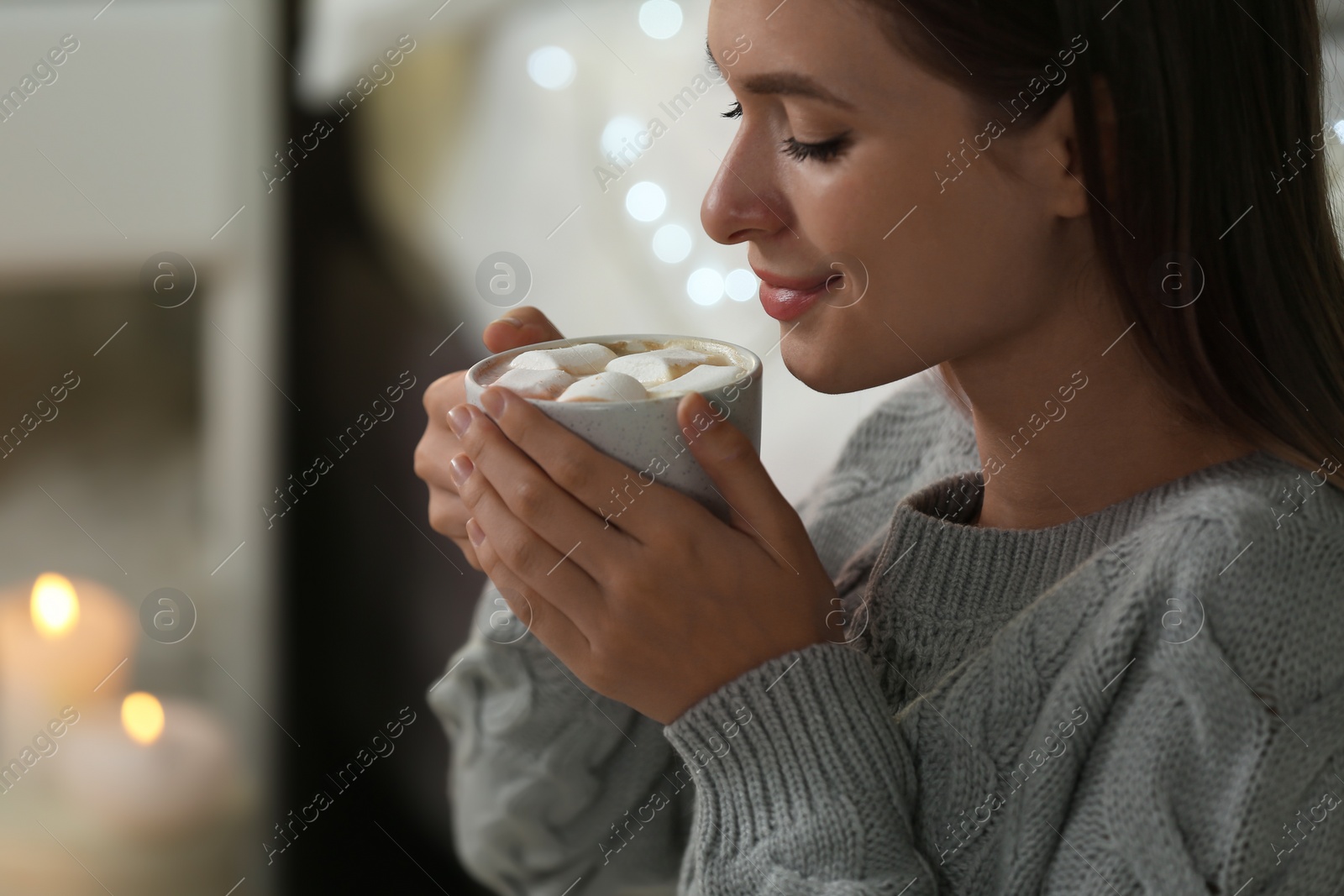 Photo of Young woman holding cup of hot cocoa with marshmallows at home. Cozy winter