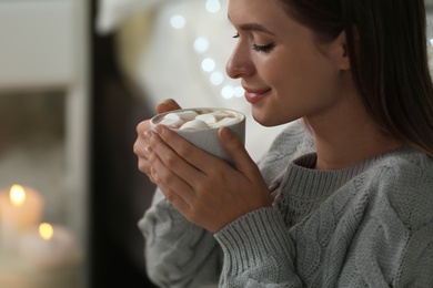 Photo of Young woman holding cup of hot cocoa with marshmallows at home. Cozy winter