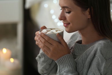 Young woman holding cup of hot cocoa with marshmallows at home. Cozy winter