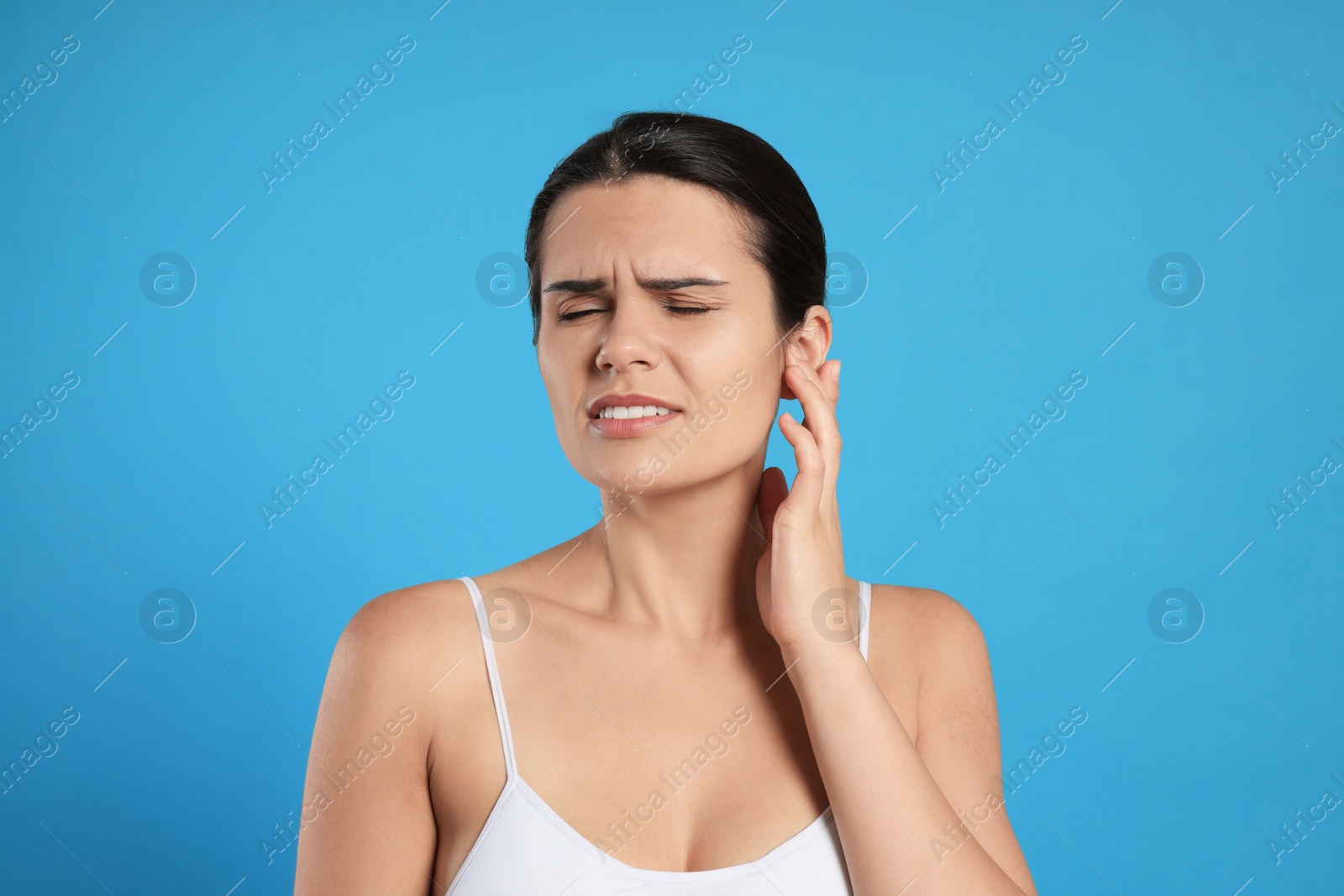 Photo of Young woman suffering from ear pain on light blue background