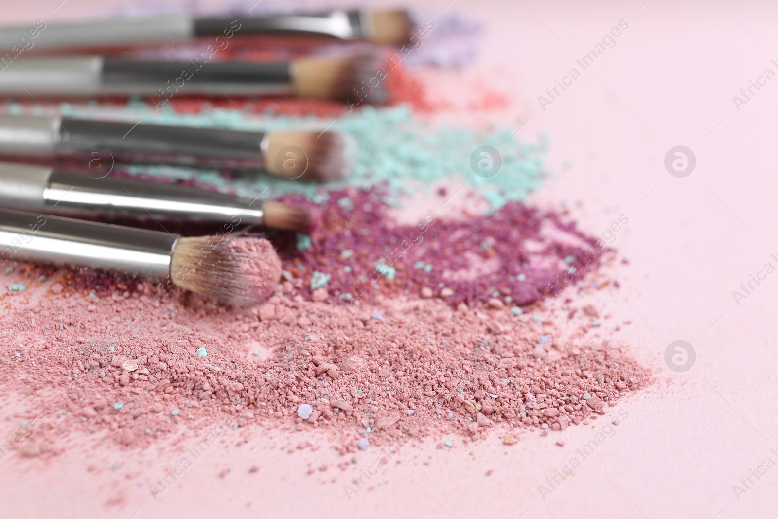 Photo of Different makeup brushes with crushed cosmetic products on pink background, closeup. Space for text