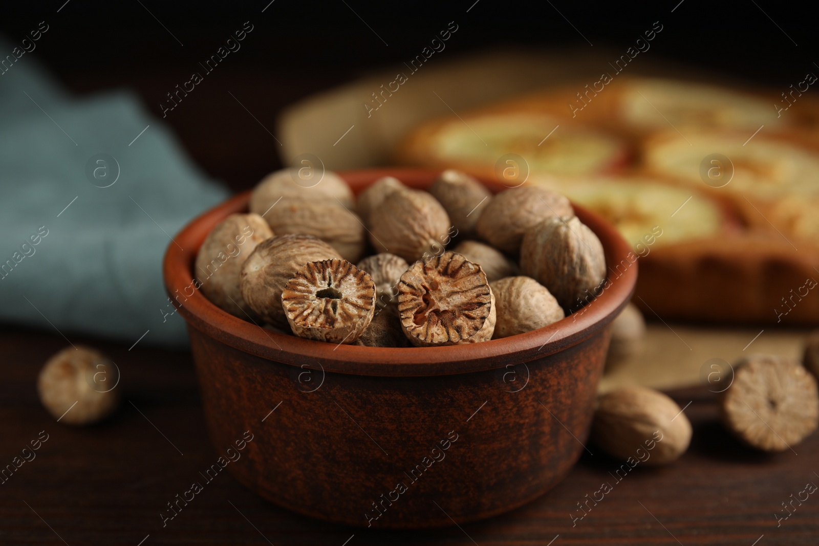 Photo of Nutmeg seeds and pie on wooden table, closeup