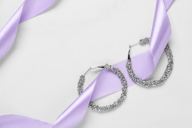 Beautiful earrings and lilac ribbon on white background, flat lay with space for text. Luxury jewelry