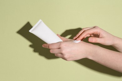 Woman with tube applying cream on her hand against green background, closeup