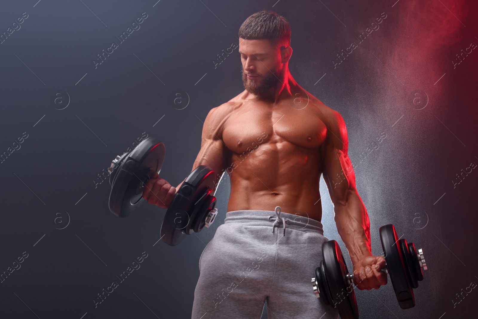 Photo of Young bodybuilder exercising with dumbbells in smoke on color background