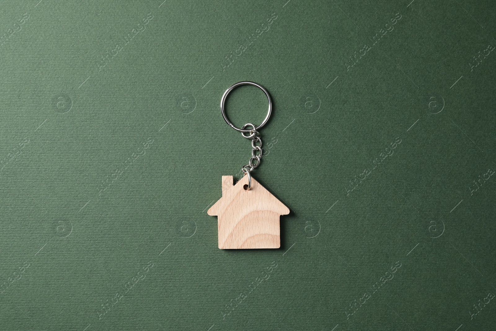 Photo of Wooden keychain in shape of house on dark green background, top view
