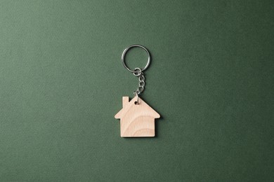 Wooden keychain in shape of house on dark green background, top view